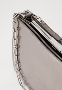 Metallisk grå lærveske med kjedehank, glatt tekstur og en strukturert design med glidelås og subtile stikk detaljer.