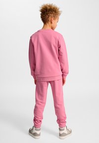 Rosa Sweatshirt und passende Jogginghose aus weicher Baumwollmischung, mit gerippten Bündchen und Bund, kombiniert mit grauen und weißen Sneakern.
