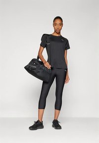 Svart atletisk t-skjorte og kaprilenggings, med en svart sportstaske. Glatt stoff, tettsittende design og subtile logo detaljer. Svarte joggesko fullfører antrekket.