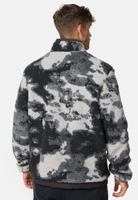Chaqueta de forro polar en patrón de camuflaje negro y gris. Cuenta con un cuello alto y una tela texturizada con un aspecto suave y aterciopelado.