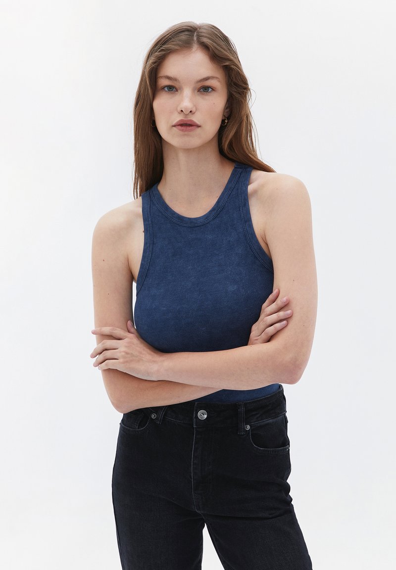 Marinblå ribbad linne med rund halsringning och ärmlös design, tillsammans med högmidjade svarta jeans. Sval yta, åtsittande stil.