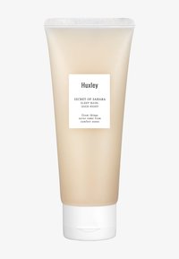 Huxley slaapmasker in een doorschijnende beige tube met een witte flip-topdop. Het etiket heeft zwarte tekst op een witte achtergrond. Gladde textuur.
