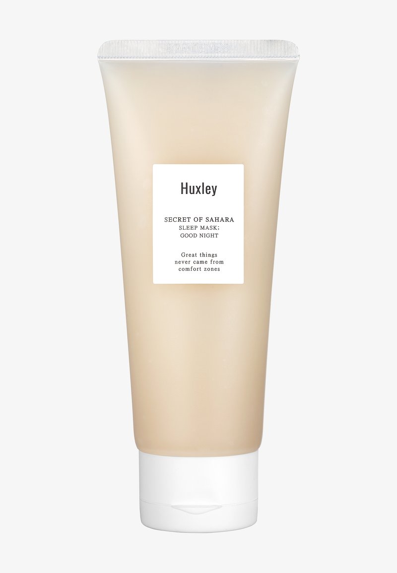 Huxley slaapmasker in een doorschijnende beige tube met een witte flip-topdop. Het etiket heeft zwarte tekst op een witte achtergrond. Gladde textuur.