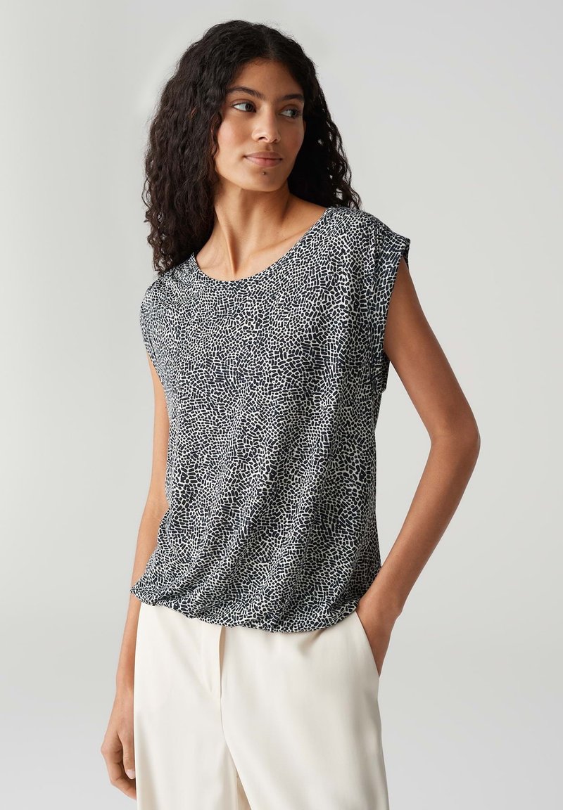 Zwart-witte short-sleeve top met een gespikkeld patroon, ronde halslijn en een relaxte fit, gecombineerd met lichtgekleurde broek.
