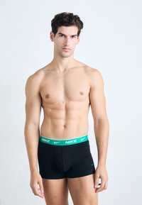 Boxer briefs negros con un logo de Nike verde y una cintura a juego, con una textura de tela suave y un diseño ajustado.