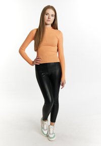 Top a maniche lunghe arancione a coste, leggings neri in similpelle e sneakers multicolori con dettagli bianchi, rosa e verdi.