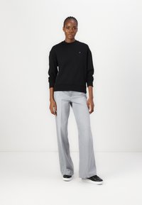 Felpa nera con maniche a costine, abbinata a jeans grigi chiari a gamba larga. Indossata con sneakers bianche e nere. Design minimalista.