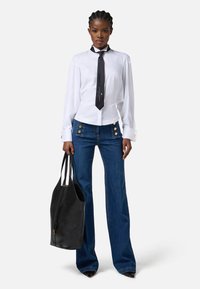 Camicia bianca a maniche lunghe con cravatta nera, abbinata a jeans di denim blu a zampa d'elefante con dettagli in bottone dorato e una borsa a tracolla in pelle nera.