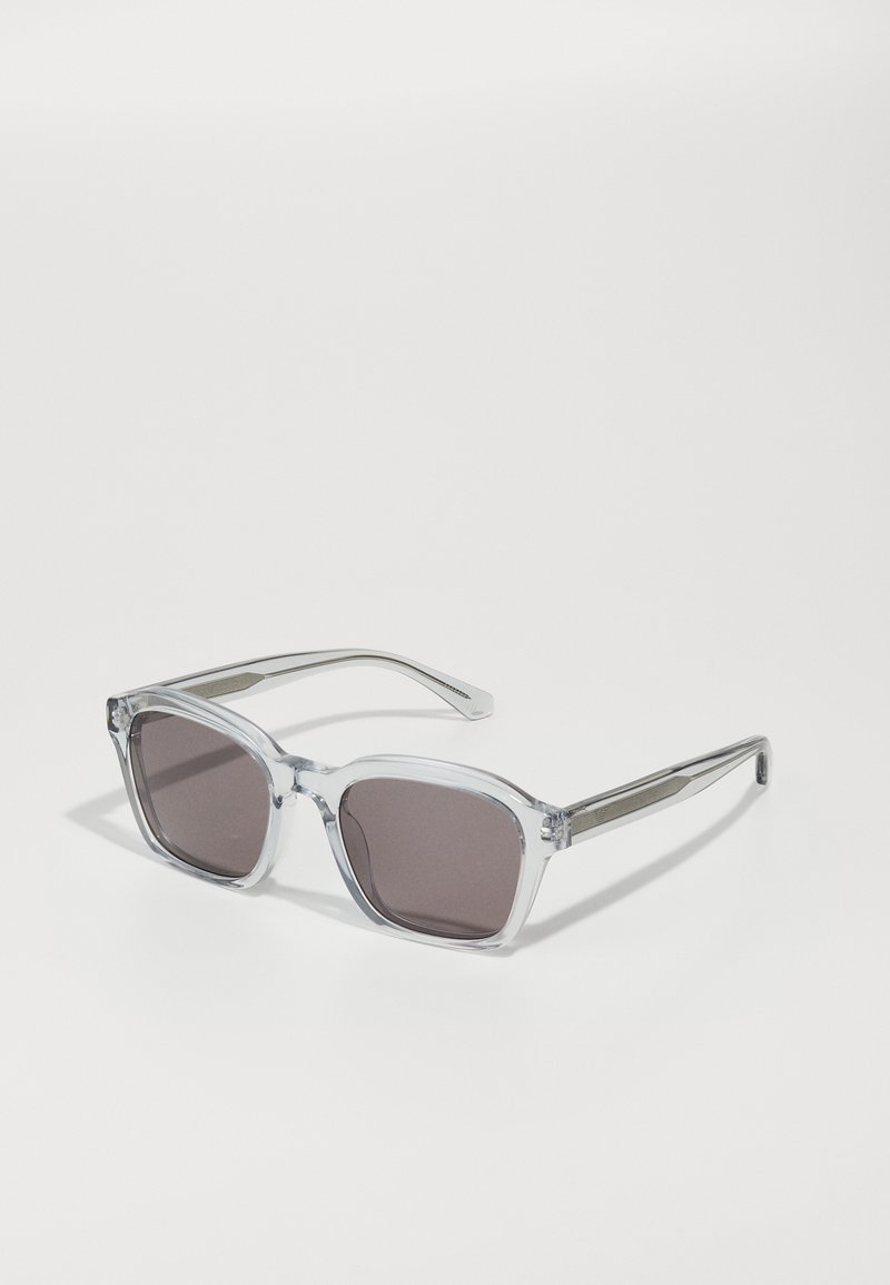 Ochelari de soare din plastic transparent cu lentile pătrate. Lentile gri, cu nuanță, accentuate de un detaliu metalic texturat pe brațe.