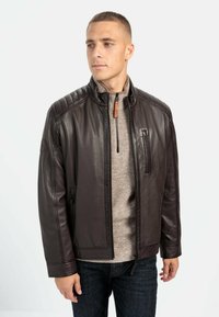 Brun læderjakke med krave, kviltet skulderdetalje og lynlås foran. Kombineret med en beige striktrøje og mørke jeans.