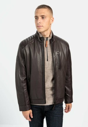 Brun læderjakke med krave, kviltet skulderdetalje og lynlås foran. Kombineret med en beige striktrøje og mørke jeans.