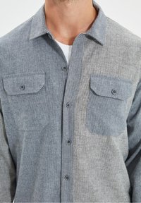 Grijs en blauw gestreept shirt van geweven textuurstof, met twee borstzakken en een knoopsluiting aan de voorkant.