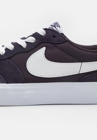 Dark purple canvas sneaker with white rubber sole, featuring white swoosh logo, flat laces, and padded collar for comfort.