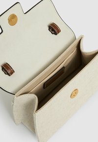 Helebeež kott tekstuurse kangaspinnaga, millel on kuldne metallist kinniti ja pruunid nahast detailid sees.