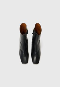 Black leather ankle boots with a squared toe, smooth texture, gold zipper accents, and a contrasting tan interior.
