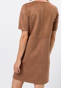 Robe en daim marron à manches courtes, avec un col rond et une silhouette cintrée, comportant des coutures verticales le long du dos pour plus de structure.
