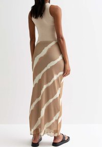 Maxi falda larga a rayas marrón y blancas hecha de tela ligera, con un dobladillo transparente y combinada con sandalias negras.