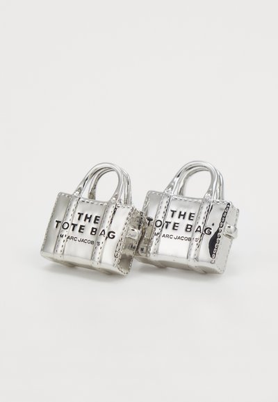 Srebrne mini torbe s utisnutim tekstom "THE TOTE BAG" i "MARC JACOBS" u crnoj boji, s malim ručkama i šivenim detaljima.