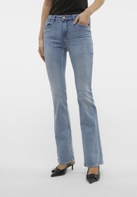 Lyseblå utsvingte jeans i denim, med høy midje, frontlommer og en utvasket finish. Kombinert med svarte spisse hæler.