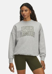 Gray sweatshirt with "UNDER ARMOUR" in black and gold lettering, loose fit, ribbed cuffs, paired with olive green bike shorts.