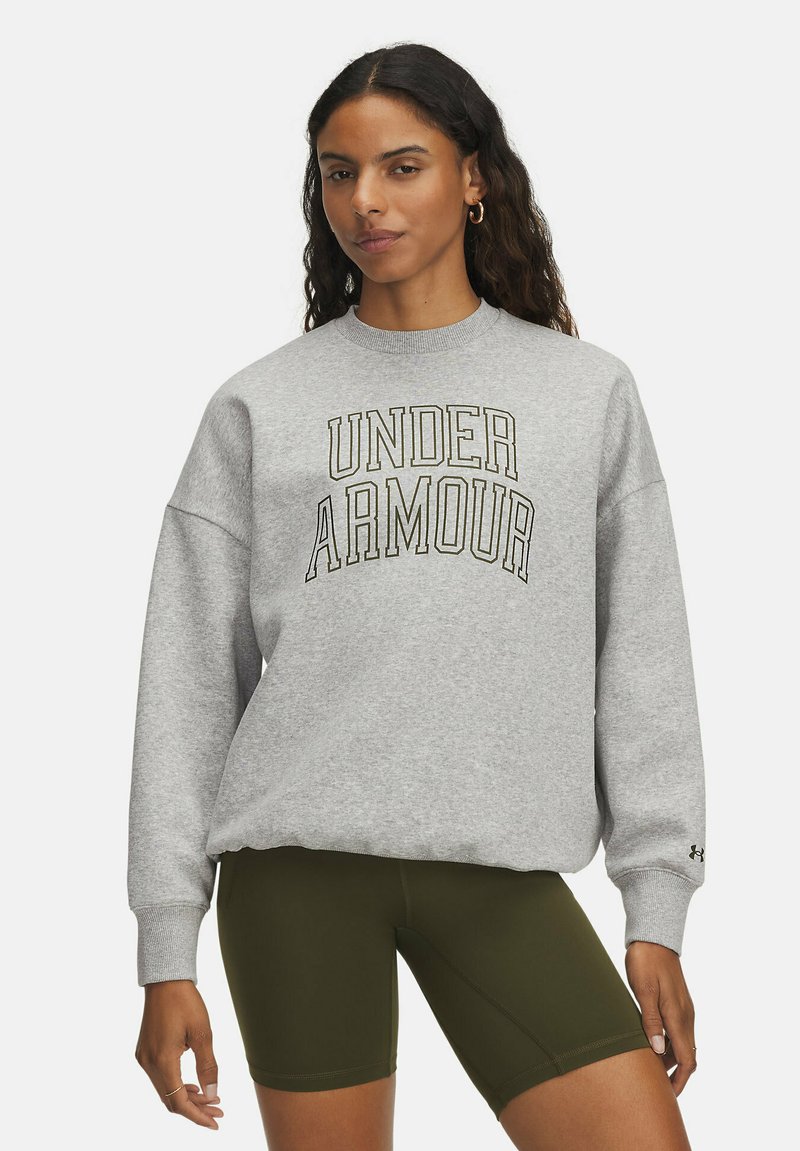 Šedá mikina s nápisom "UNDER ARMOUR" v čiernej a zlatej farbe, vo voľnom strihu, s rebrovanými manžetami, skombinovaná s olivovozelenými cyklistickými šortkami.