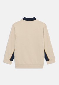 Sudadera beige de manga larga, con cuello azul marino y paneles laterales azul marino. Presenta una textura suave y puños acanalados en las mangas y el dobladillo.