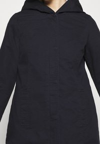 Giacca con cappuccio blu navy realizzata in tessuto leggero, con chiusura frontale a bottoni e due tasche laterali. Texture liscia, design slim fit.