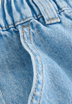 Tekstura jasnoniebieskiego denimu, z marszczoną gumką w talii, pomarańczowym przeszyciem oraz miękkim, lekko wyblakłym wyglądem z widocznym wzorem tkaniny.