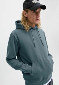 Kapuzenshirt in gedämpftem Blaugrün, aus weichem Stoff. Verfügt über eine Fronttasche, gerippte Bündchen und verstellbare Kordeln.