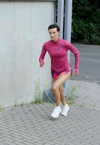Sportoutfit in lebhaftem Pink, kurzärmliges Oberteil mit Reißverschluss, kombiniert mit passenden Shorts und weißen Sneakers, läuft auf Ziegelpflaster.