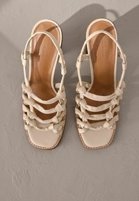 Sandales à talons blanches en cuir avec un design de brides tissé, bout carré et semelle intérieure beige avec des détails de couture.