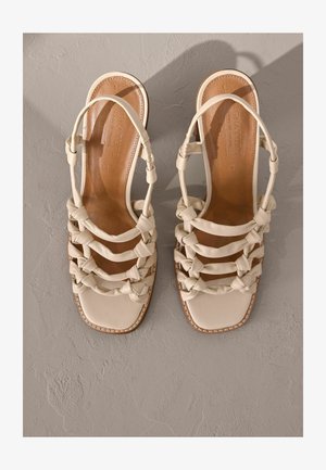 Sandales à talons blanches en cuir avec un design de brides tissé, bout carré et semelle intérieure beige avec des détails de couture.