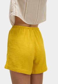 Shorts amarillos de textura con cintura elástica y bolsillos laterales, hechos de una tela ligera, que presentan un ajuste relajado y una longitud a mitad del muslo.