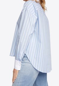 Hellblau gestreiftes Button-Up-Hemd mit weißen Manschetten und abgerundetem Saum. Der Stoff hat eine glatte, feste Textur.