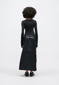 Μαύρο τοπ με μακριά μανίκια και αντιθετικές ραφές, συνδυασμένο με μαύρη φούστα ψηλόμεση που έχει το κείμενο "NIKE SHOX" στη μέση.