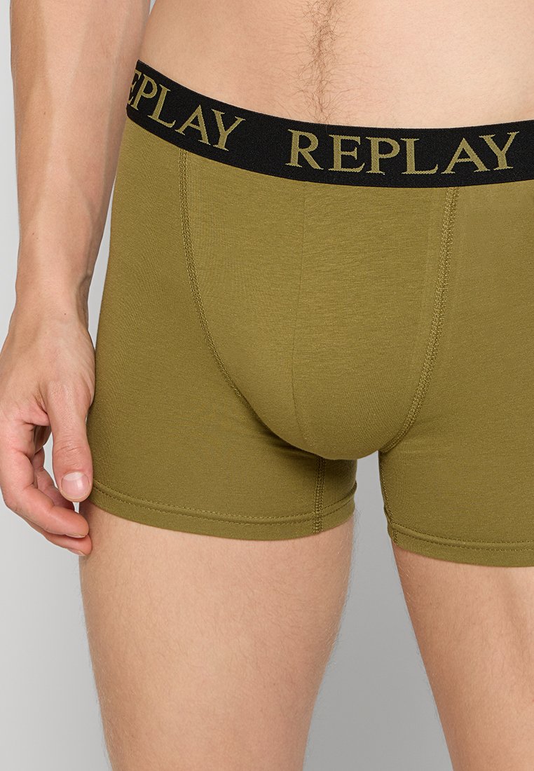 Gröna herrboxer med svart midjeband som har "REPLAY"-logotypen, bärs av en manlig modell mot en neutral bakgrund.