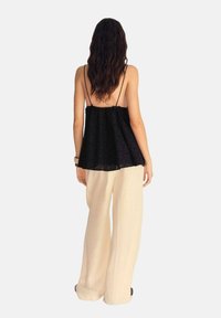 Camisola in pizzo nero con spalline sottili, design morbido, abbinata a pantaloni beige chiaro a gamba larga, vista da dietro.