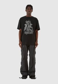 Sort oversized t-shirt med et gråt grafisk tryk af en kvinde og teksten "mgonzales", parret med mørke cargo bukser og sorte sneakers.