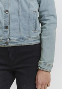 Ljust blå denimjacka med en figurnära passform, som har fyra knappar, en bröstficka och ärmar med sydda detaljer.