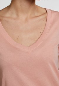 Różowa koszulka V-neck wykonana z miękkiego materiału, charakteryzująca się gładką fakturą i prostym krojem z starannie przeszytym dekoltem.