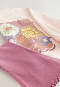 Sweat-shirt rose doux avec des illustrations colorées de soleil, lune, étoile et fleur, associé à un pantalon mauve côtelé avec des poignets à volants.
