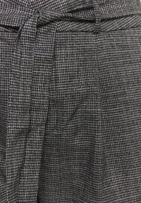 Šedá kostkovaná látka s texturovaným tkaním, s vázacím pásem v pase a sklady pro větší objem.