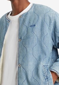 Džínová bunda v světle modré barvě s vlnitým šitím, zapínání na knoflíky a logo Levis na hrudi, s měkkou podšívkou a texturovanými manžetami.
