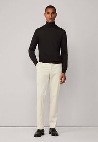 Zwarte coltrui, aansluitend, gecombineerd met crèmewitte slim-fit broek en zwarte nette schoenen. Minimalistisch ontwerp, effen kleuren.