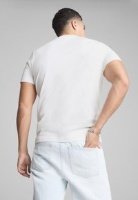 Camiseta de algodón blanca con mangas cortas, de forma ajustada y textura suave, combinada con vaqueros de mezclilla azul claro que tienen dos bolsillos traseros.