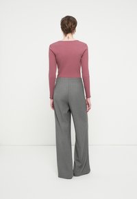 Langermet, ribbet mauve topp paret med høylivede, vide grå bukser, som har en jevn tekstur og skreddersydd design.