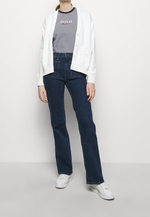 Cárdigan blanco de punto con botones sobre una camiseta de rayas azul marino, combinado con jeans de tiro alto en azul oscuro y zapatillas blancas.