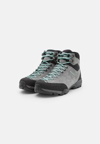 Bottes de randonnée grises avec semelles en caoutchouc noires, lacets turquoise, et un mélange de cuir suédé et de matière synthétique pour le dessus. Comprend un renforcement au niveau des orteils et un soutien de la cheville.