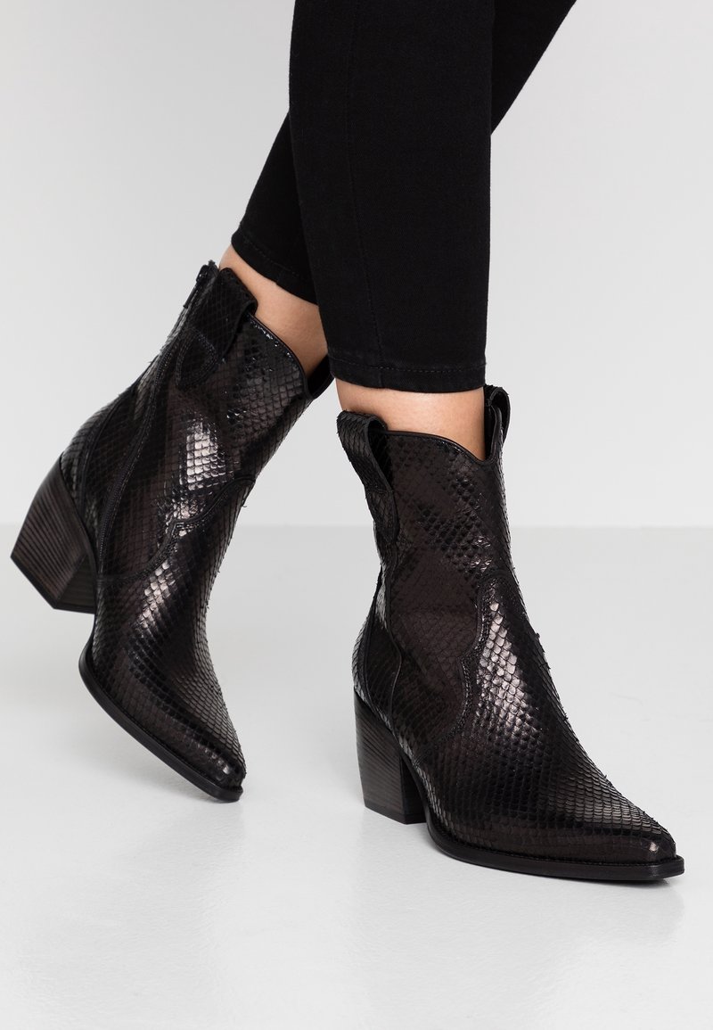 Bottines noires en simili cuir serpent, à bouts pointus, avec un talon empilé et des panneaux élastiques sur les côtés, présentant une surface texturée et des détails western.