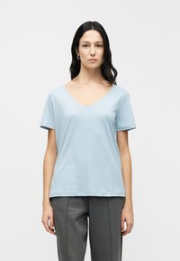 Ανοιχτό μπλε βαμβακερό T-shirt με V-λαιμόκοψη και κοντά μανίκια, χαλαρή εφαρμογή και λεία υφή, συνδυασμένο με γκρι φόρμα.